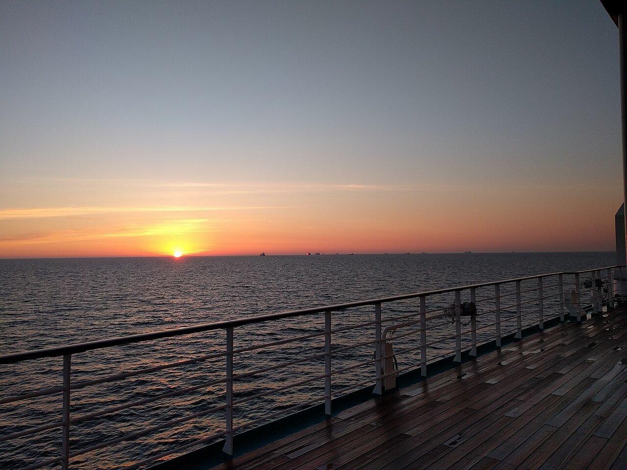 The sun setting over a calm sea, seen from the teak promenade deck of a cruise ship.