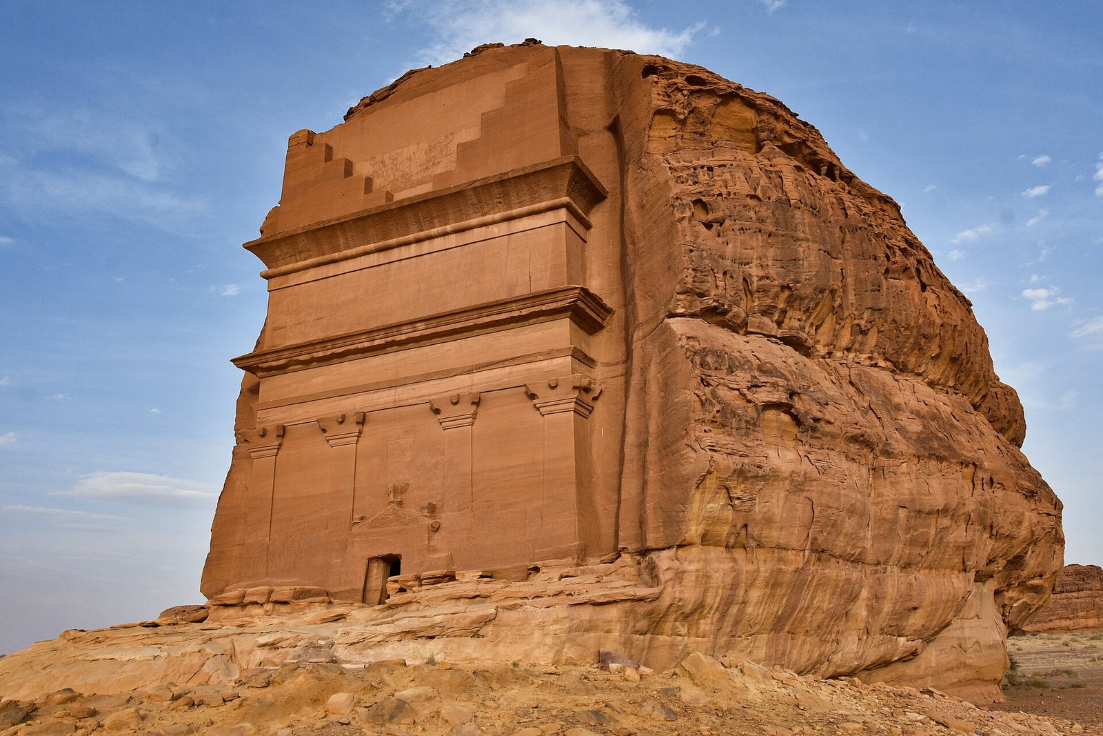 Qasr al-Farid, the lone Nabataean tomb carved into a sandstone outcrop at Hegra in AlUla, under a blue sky.