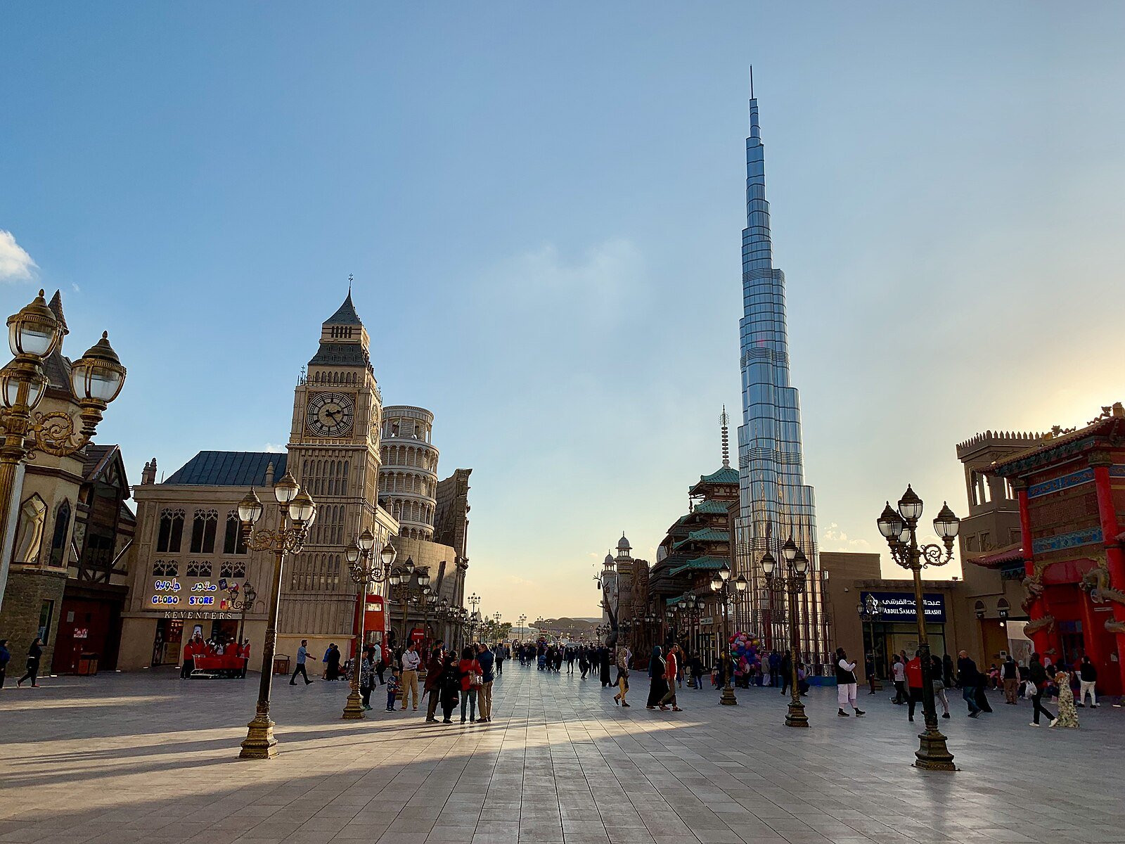 Global Village in Dubai in late-afternoon light, its lamp-lined promenade leading past ornate replica towers.