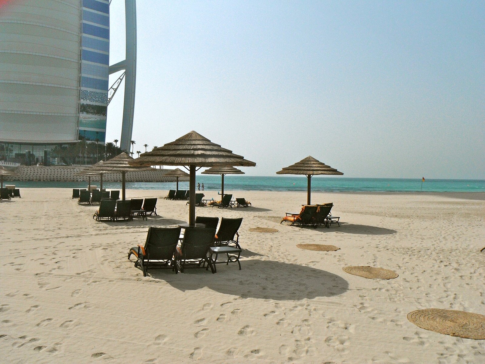 Thatched parasols and sun loungers on the sand of Jumeirah Beach beside the Burj Al Arab, Dubai.