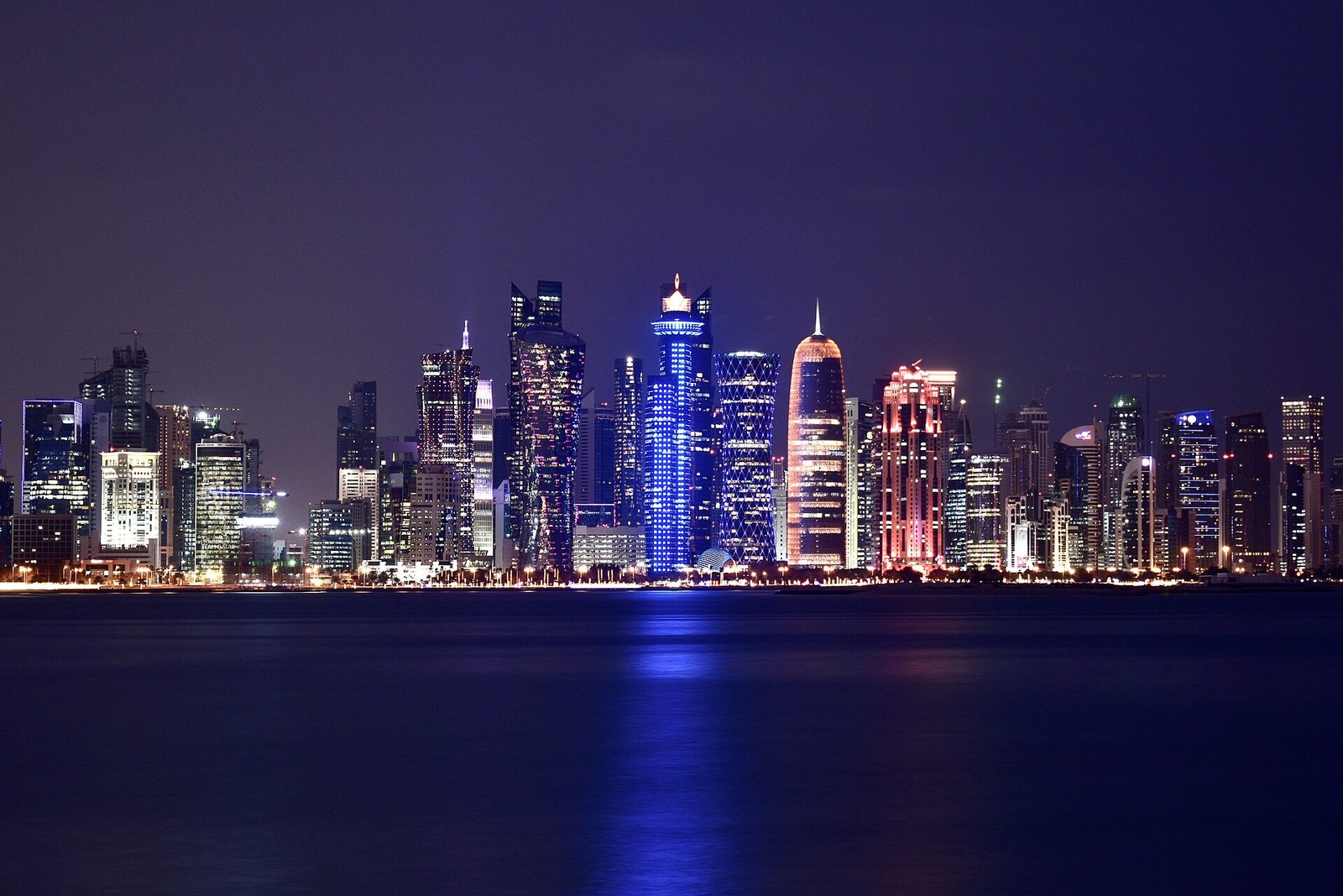 The towers of Doha's West Bay lit up at night and reflected across the bay.