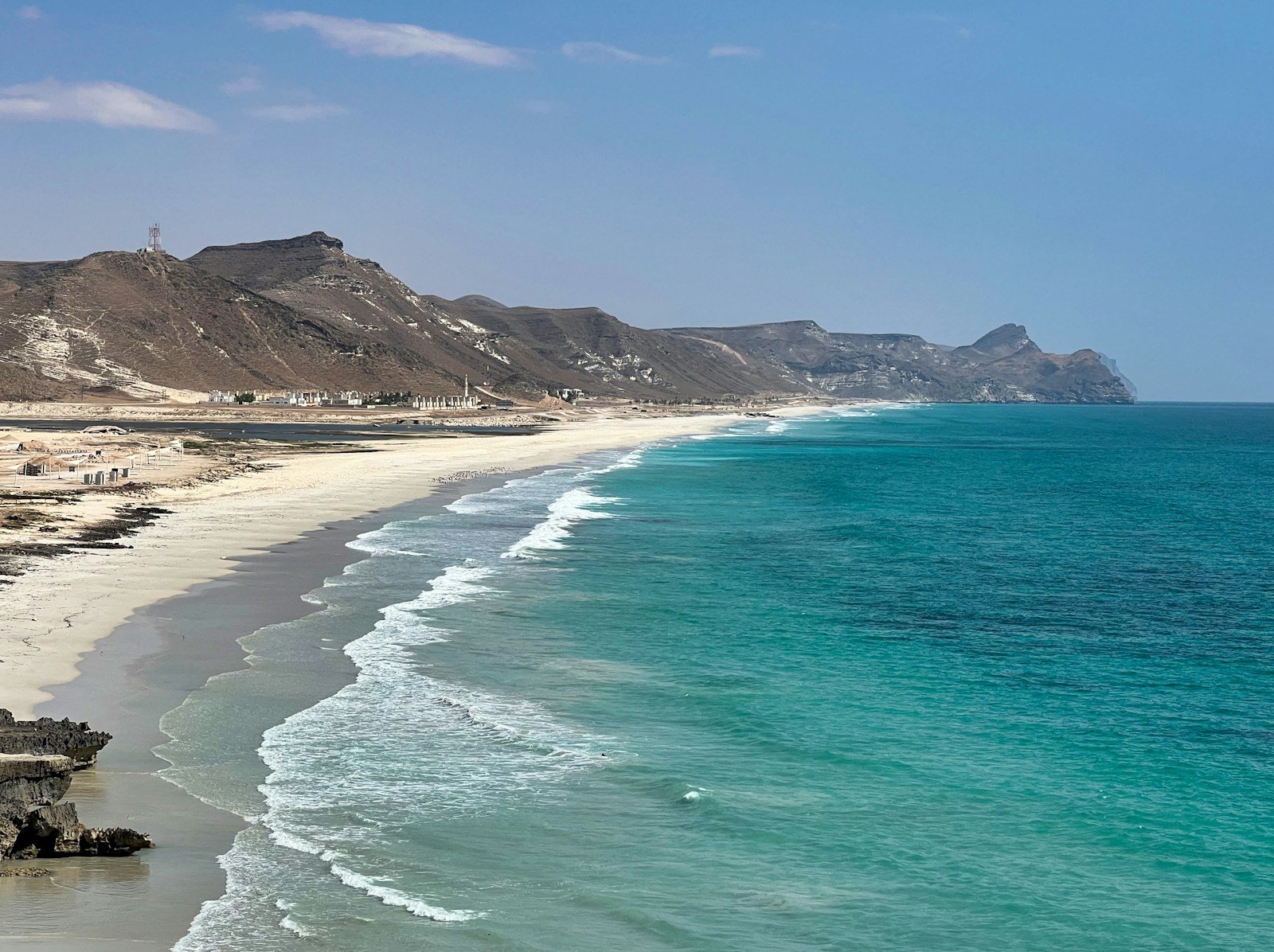 A long white-sand beach and turquoise surf beneath the mountains near Salalah, Oman