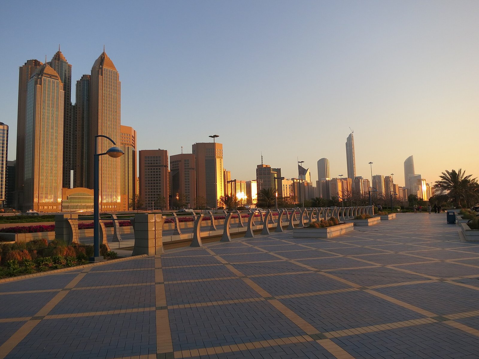 The towers of the Abu Dhabi Corniche glowing in golden evening light above the waterfront promenade.