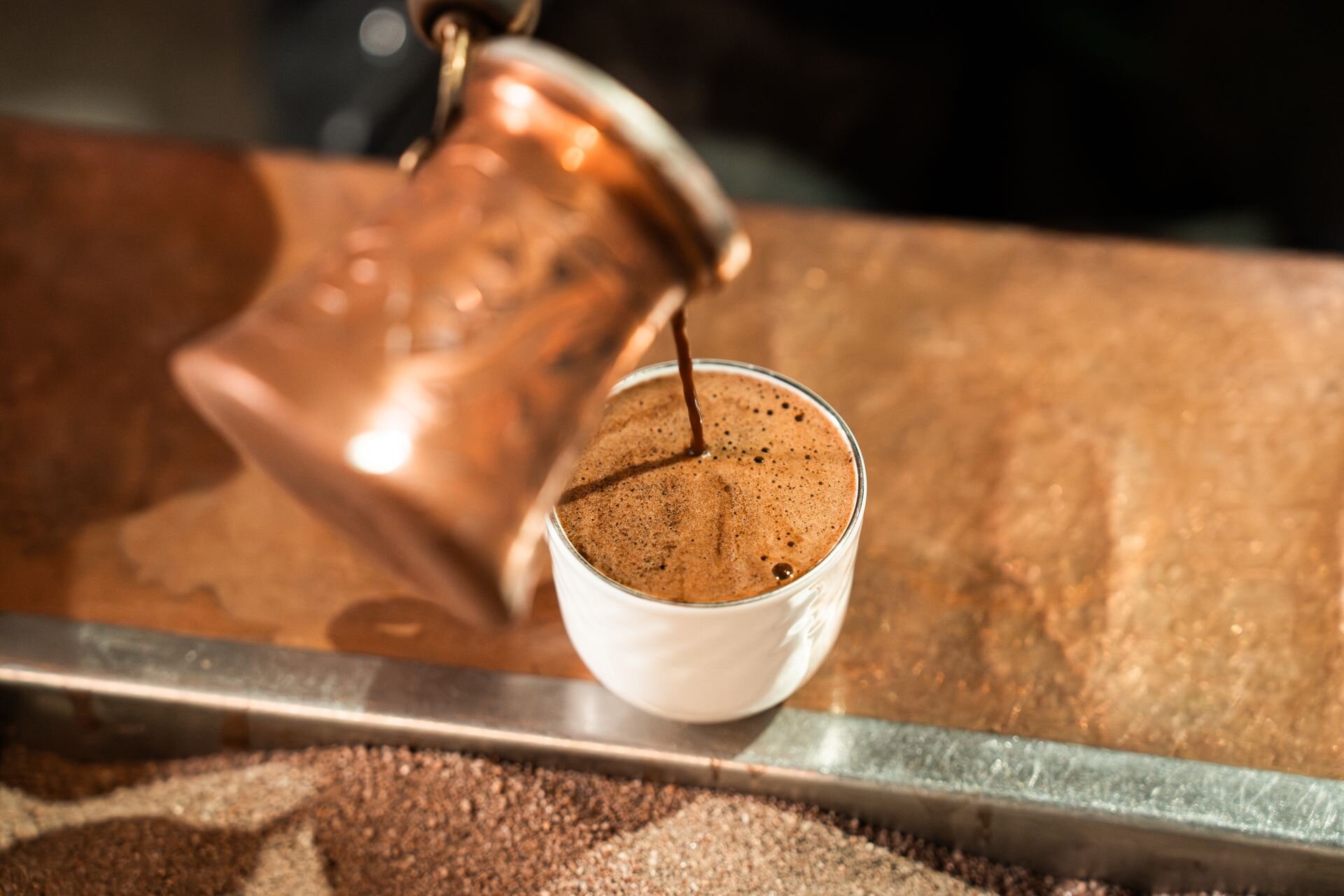 Arabic coffee poured from a copper pot into a small white cup