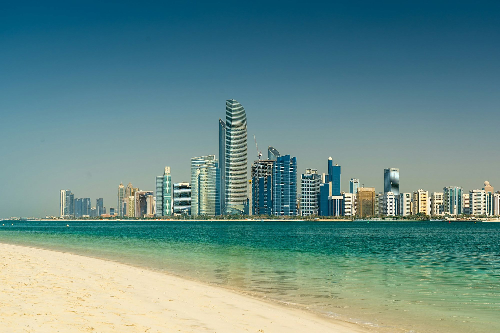 The towers of Abu Dhabi rising across turquoise water from a white sand beach
