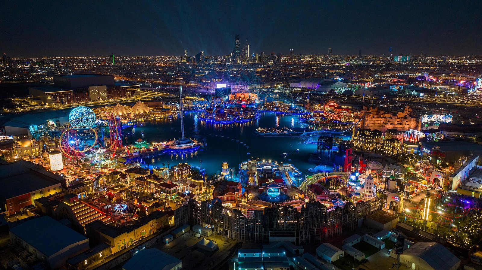 Boulevard World in Riyadh glowing at night around its lake, with the city skyline beyond