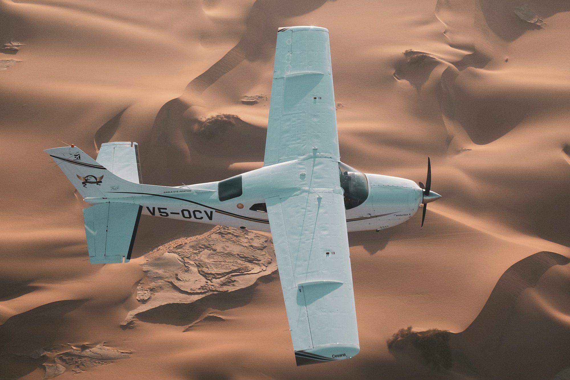 A light aircraft flying low over golden desert dunes