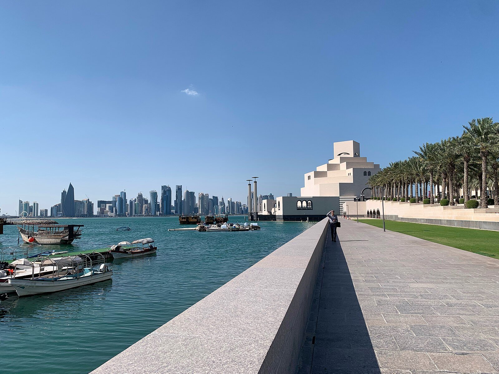 Traditional dhows moored below the Museum of Islamic Art, with the towers of Doha's West Bay across the bay.