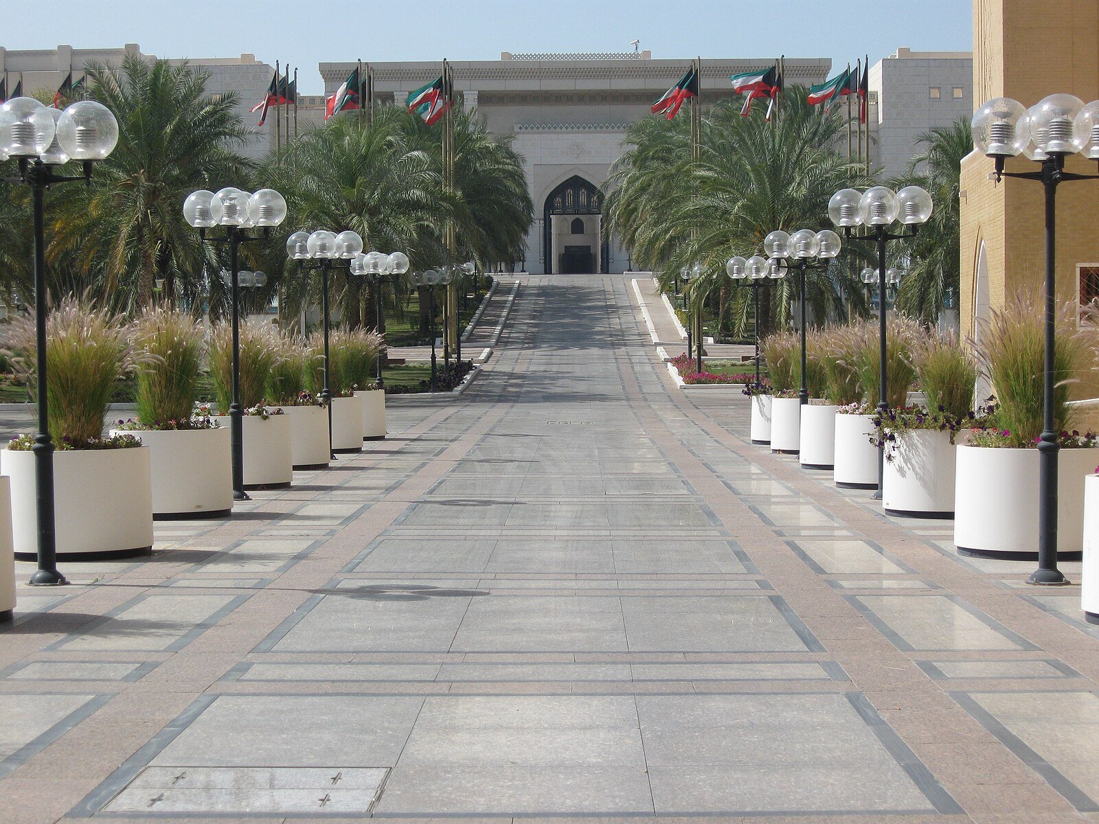 A palm-lined approach with lanterns and Kuwaiti flags leading to Seif Palace in Kuwait City.