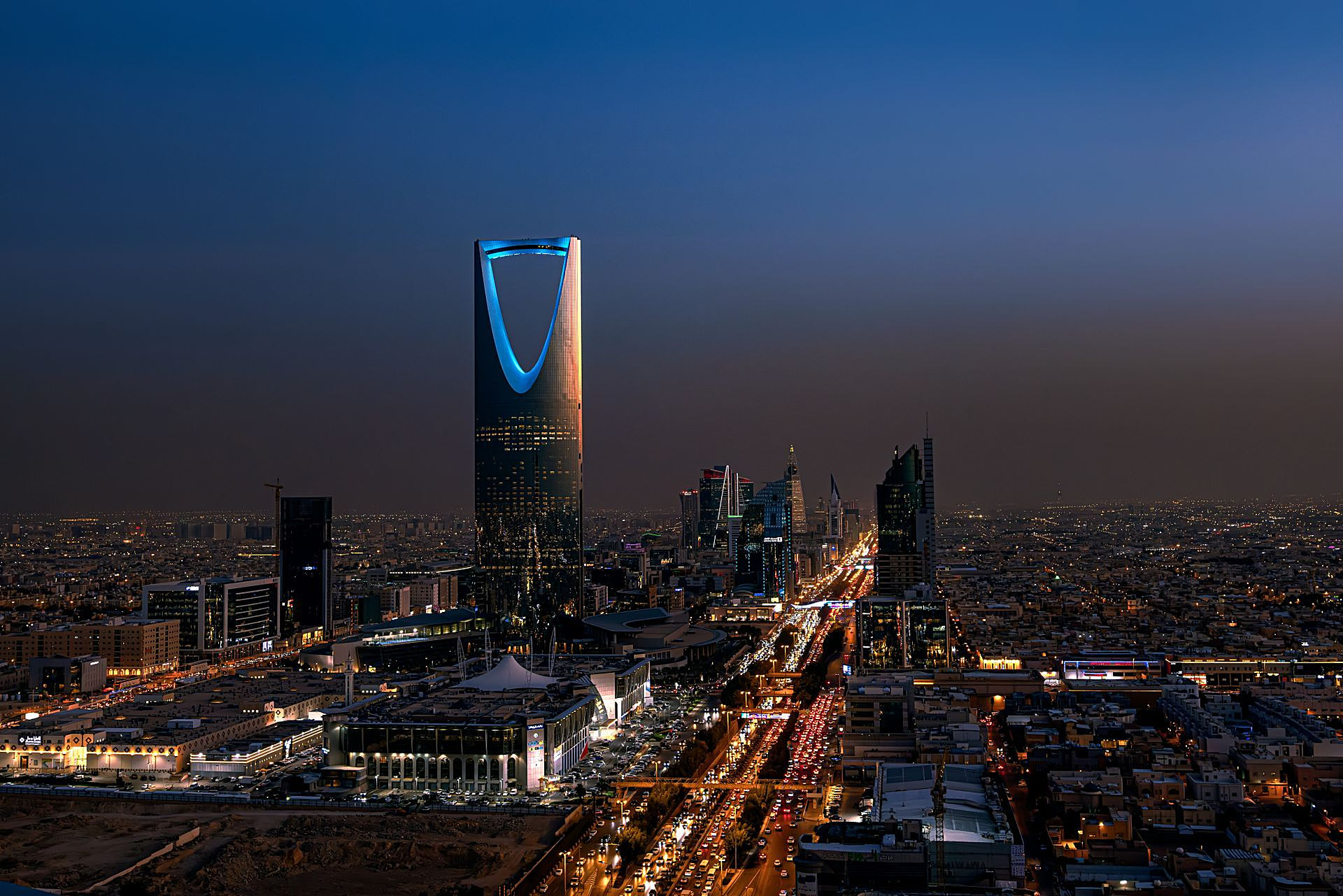 Kingdom Centre lit blue above Riyadh at dusk, with King Fahd Road glowing with traffic
