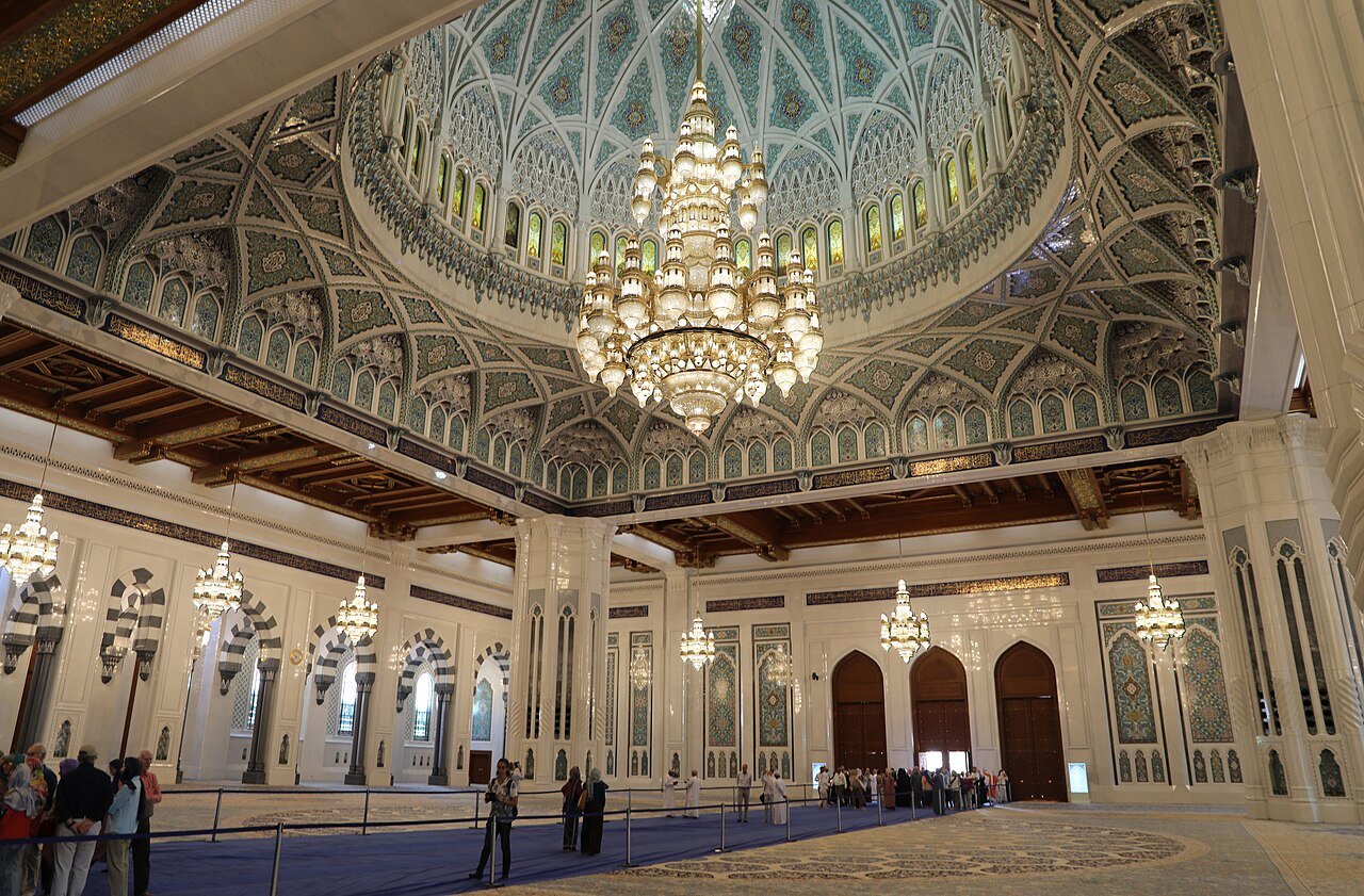 The prayer hall of the Sultan Qaboos Grand Mosque in Muscat, beneath its carved dome and great crystal chandelier.
