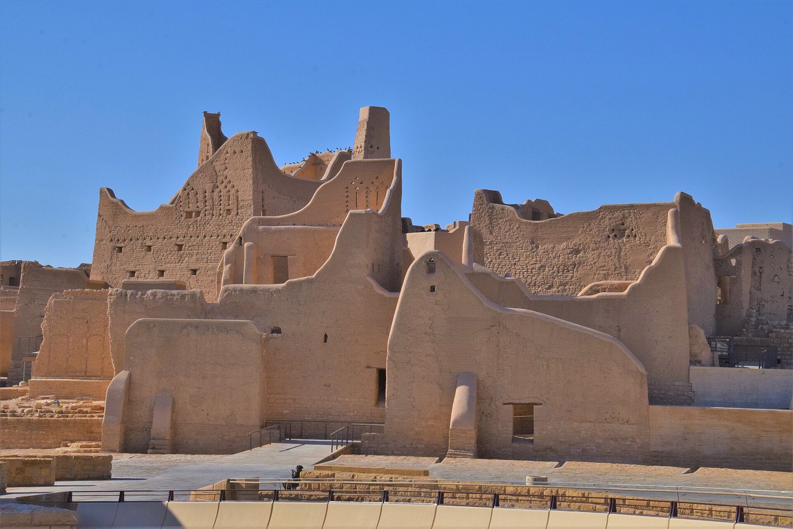 The mud-brick walls and towers of Salwa Palace in the At-Turaif district of Diriyah under a clear blue sky.