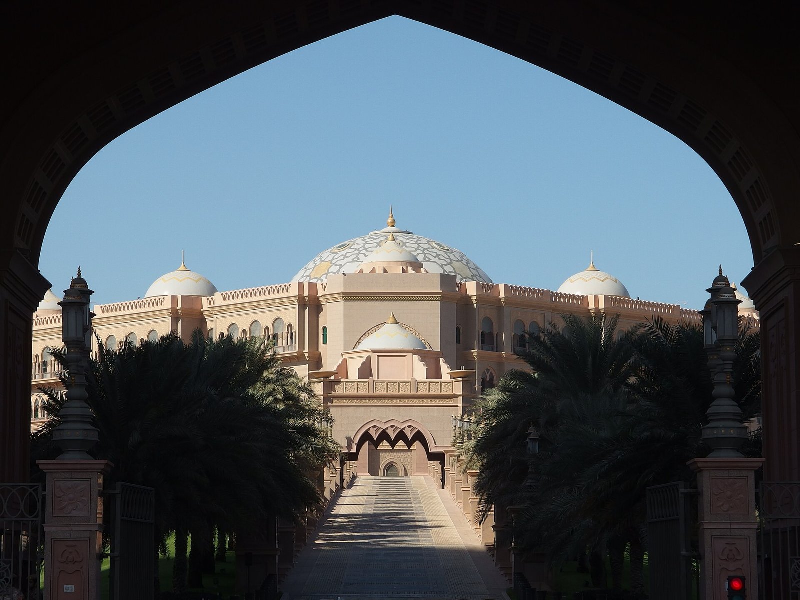 Emirates Palace and its domes framed by a pointed arch at the end of a palm-lined approach, Abu Dhabi.
