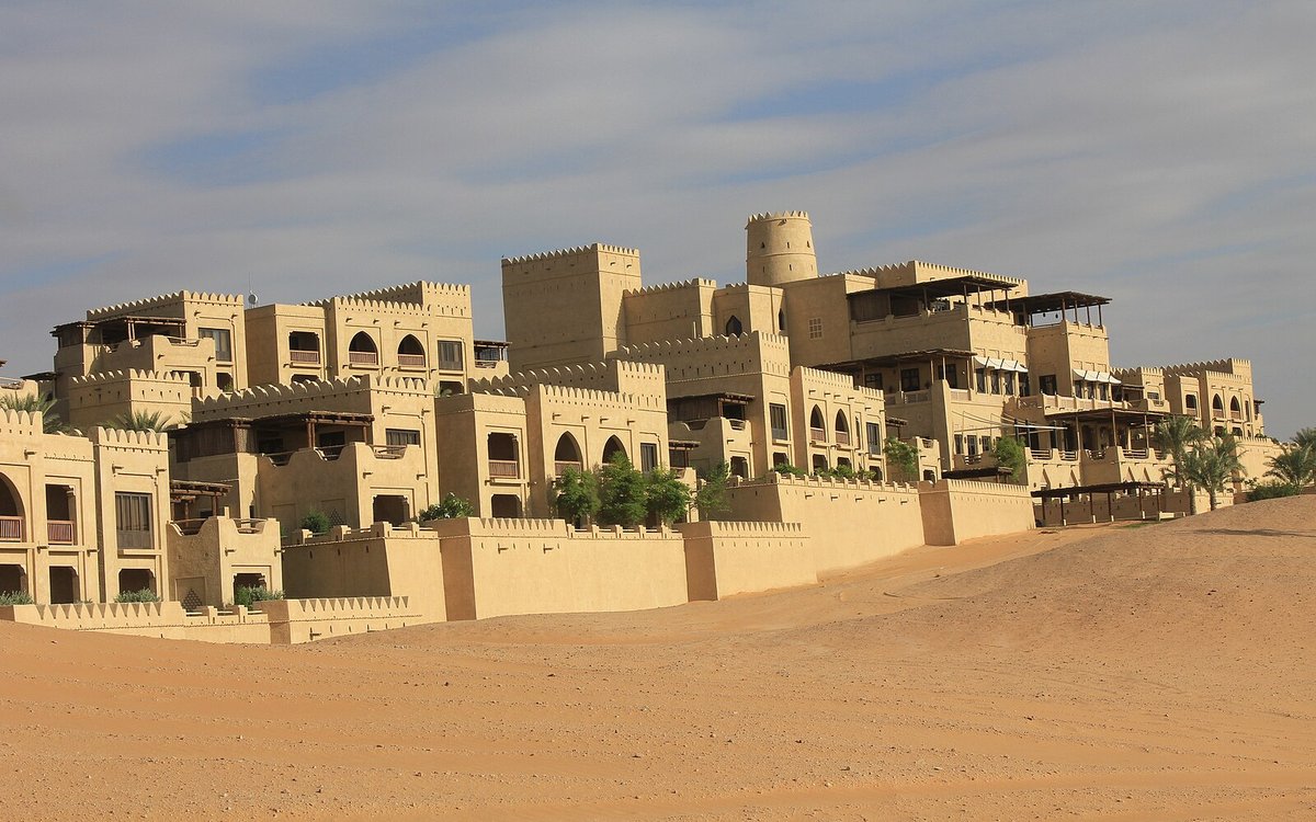The sand-coloured battlements and terraces of Qasr Al Sarab rising from the dunes of the Liwa desert