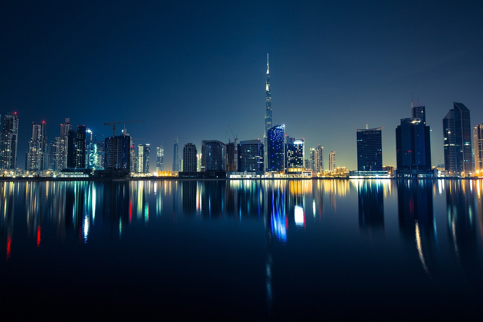 The Dubai skyline and the Burj Khalifa reflected in still water at night.