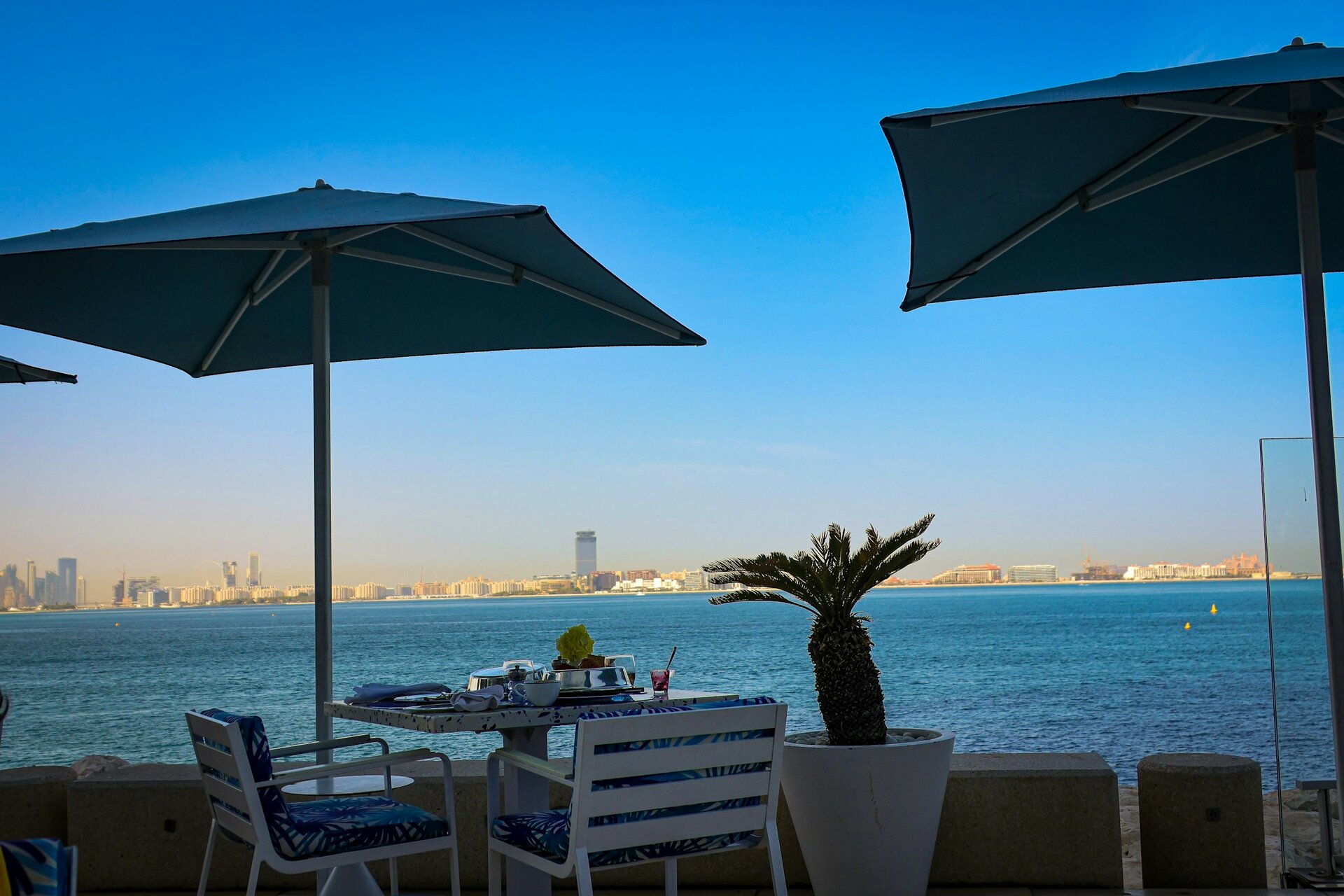 A table set beneath parasols on a seafront terrace, looking across to the Palm Jumeirah, Dubai