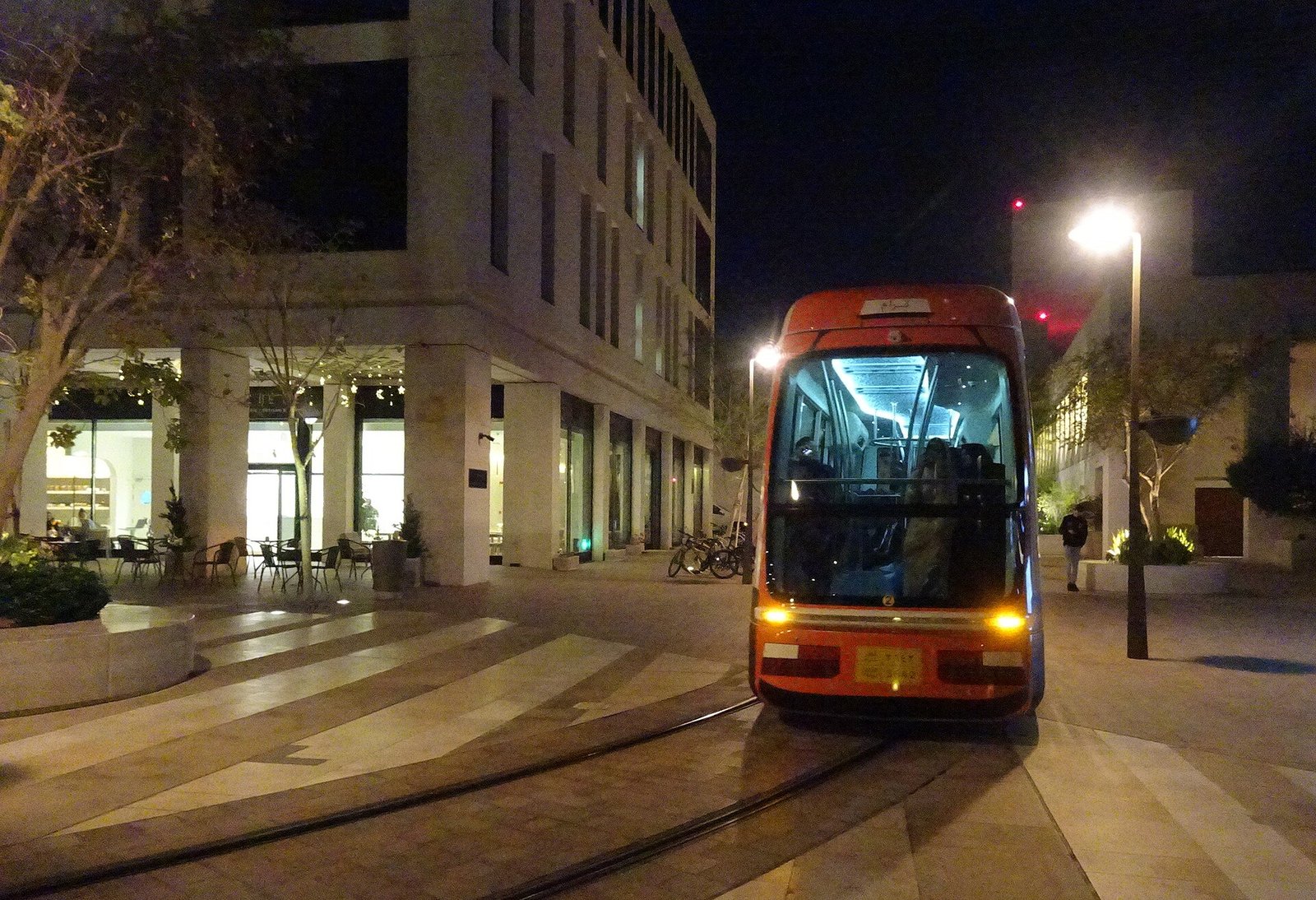 The Msheireb tram gliding along a lamplit, stone-paved street in Msheireb Downtown Doha at night.