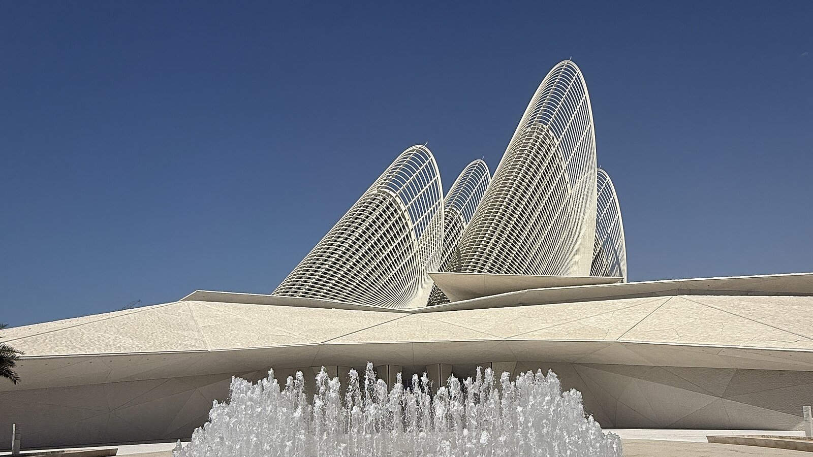 The falcon-feather towers of the Zayed National Museum rising above a fountain on Saadiyat Island under a deep-blue sky