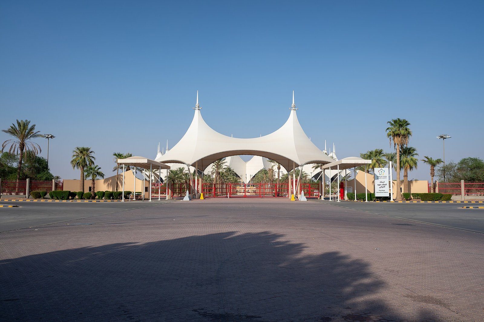 The white tented gateway of King Fahd International Stadium in Riyadh, lined with palms under a clear sky.