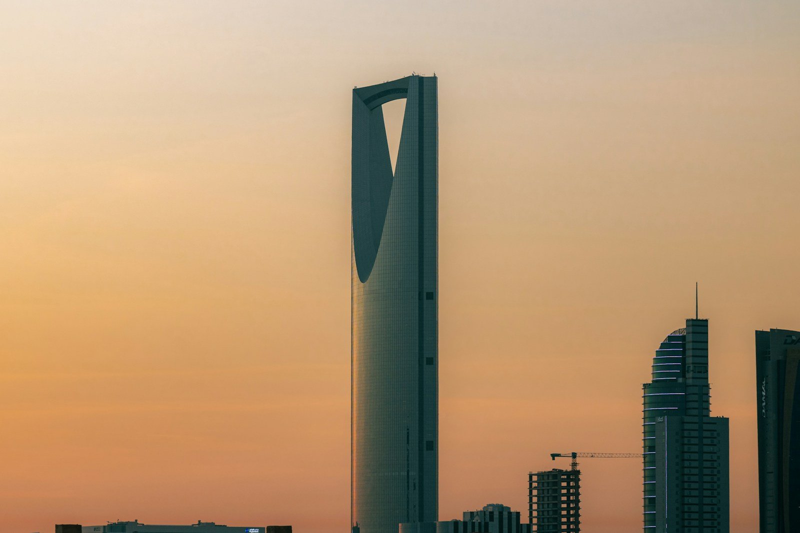 The Kingdom Centre tower silhouetted against a warm amber sky at sunset in Riyadh.