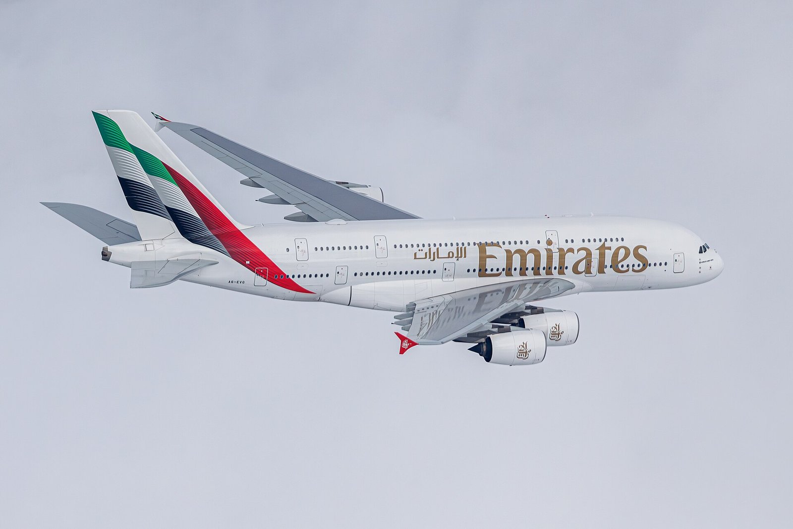 An Emirates Airbus A380 in flight, its double deck and red, green and black tail livery against a pale sky.