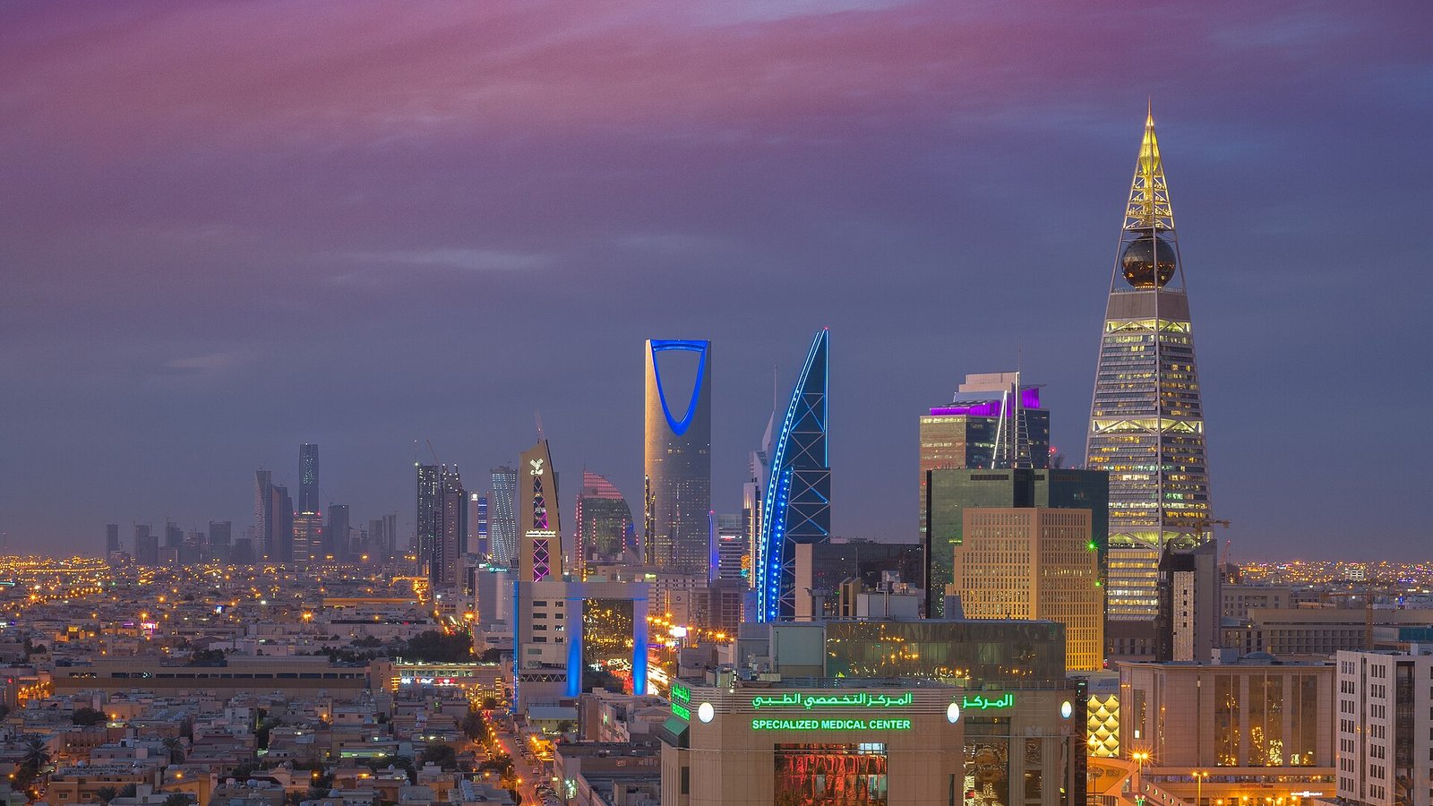 The Riyadh skyline at dusk, with the Kingdom Centre and Al Faisaliah towers lit against a violet sky.