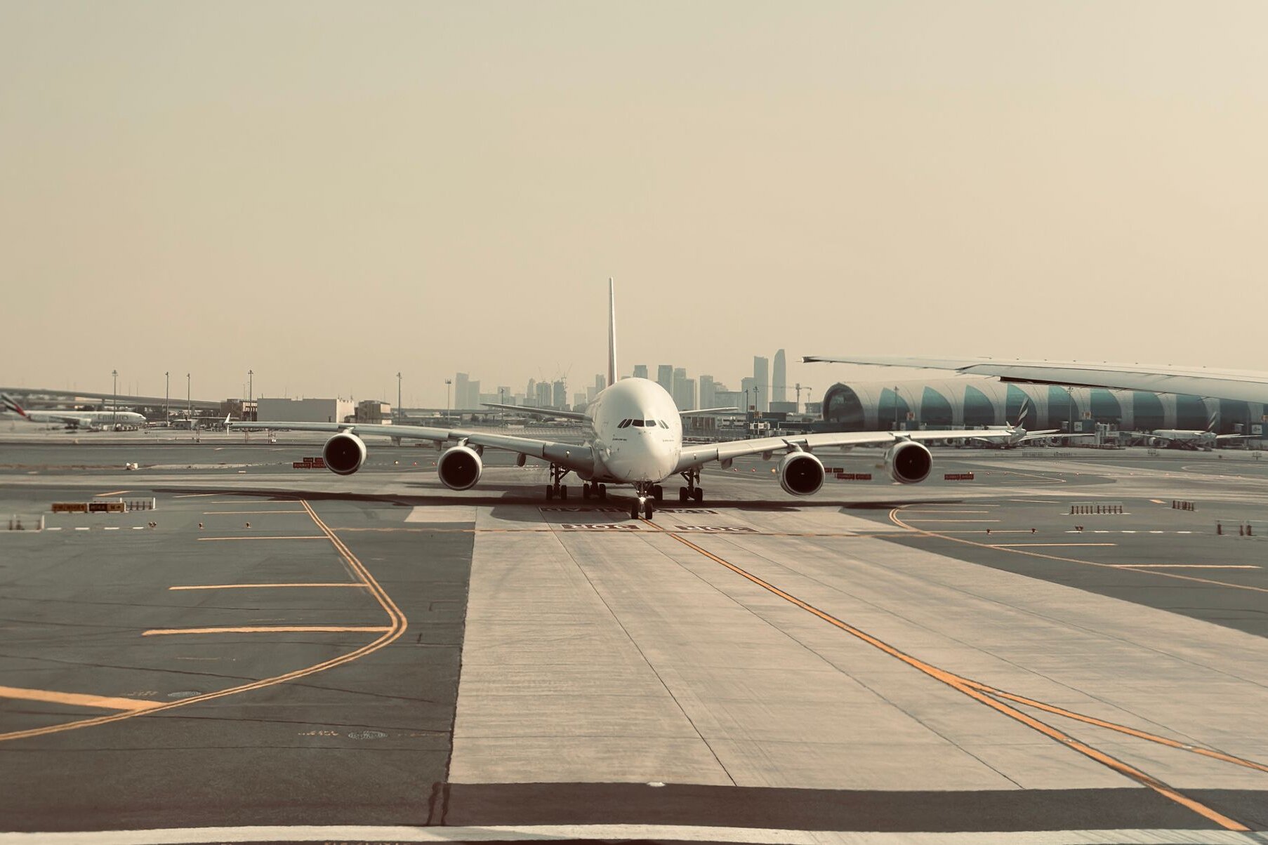 An Emirates A380 taxiing at Dubai International Airport, the city's towers behind