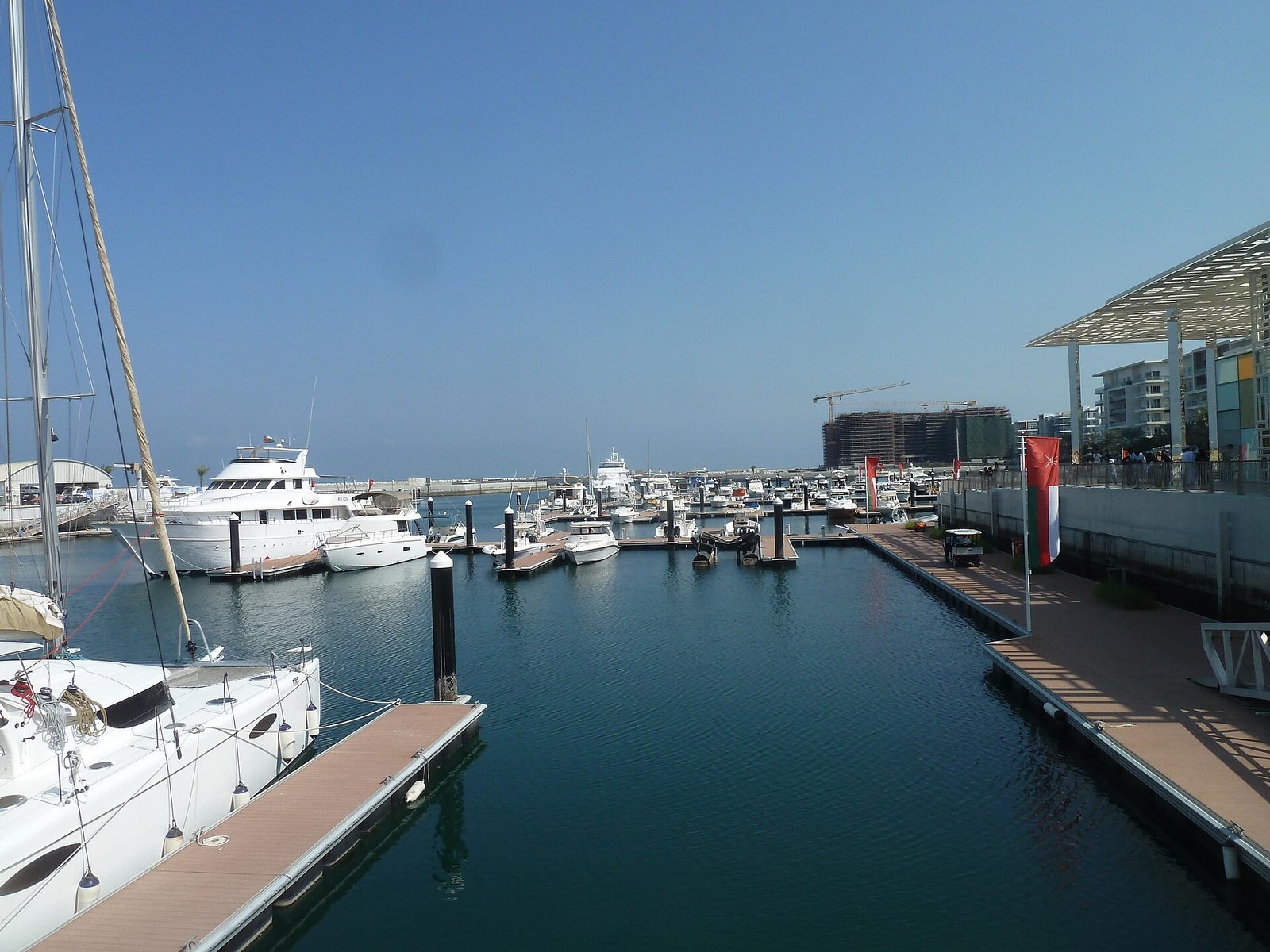 Yachts berthed along the pontoons of Al Mouj Marina, Muscat's waterfront residential district, under a clear sky.