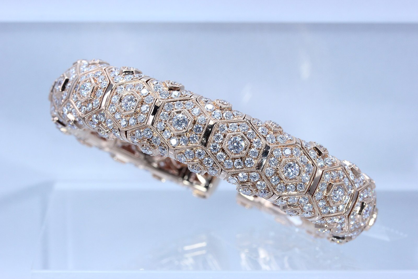 A rose-gold bracelet set with hexagonal clusters of diamonds, displayed against a pale blue ground.