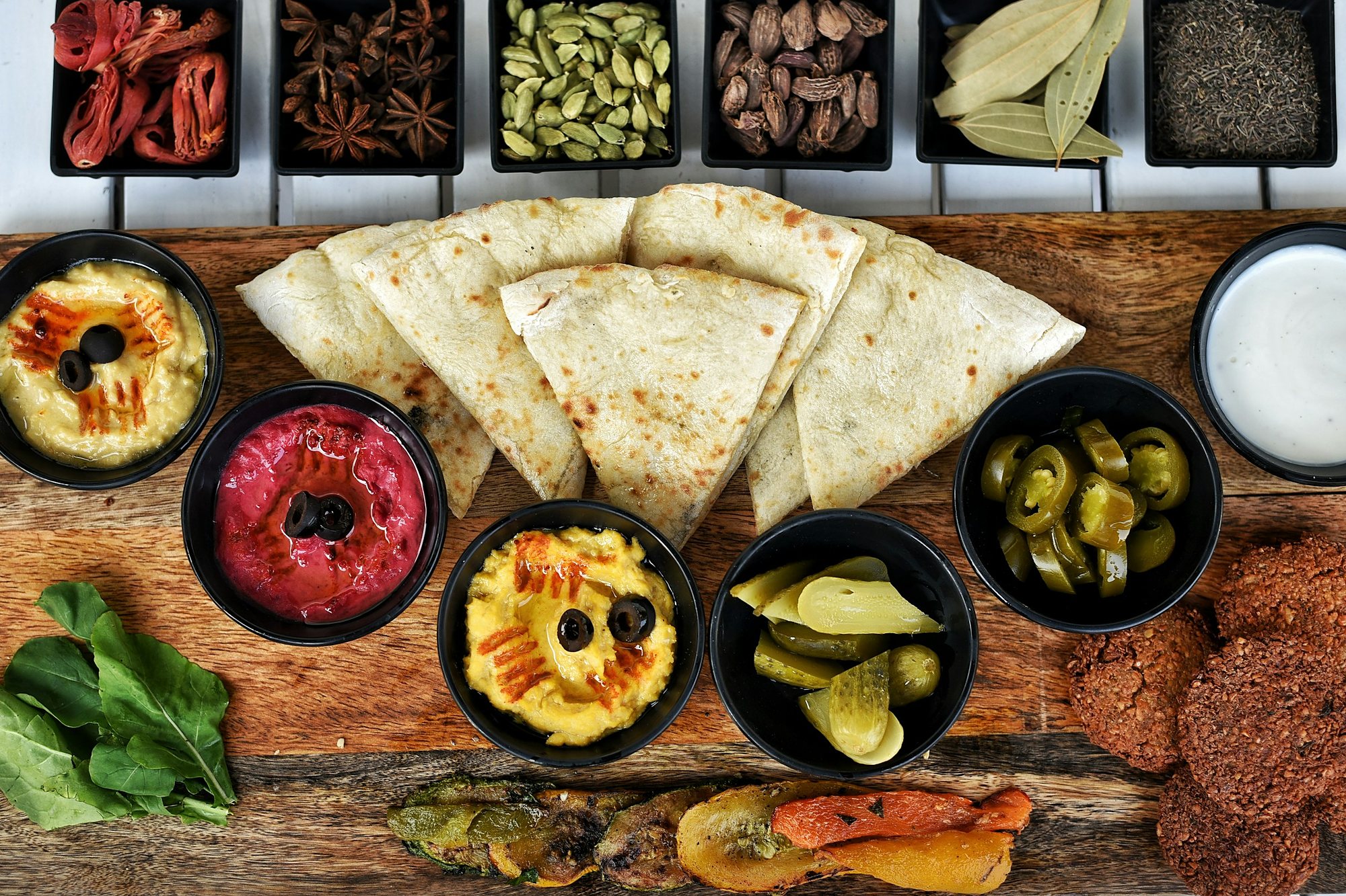Hummus, beetroot dip, pickles, falafel and warm bread with bowls of whole spices