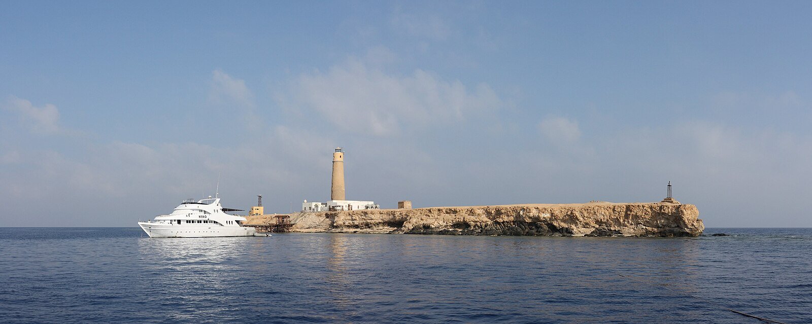 A white motor yacht lies off Big Brother Island and its old stone lighthouse in the open Red Sea.