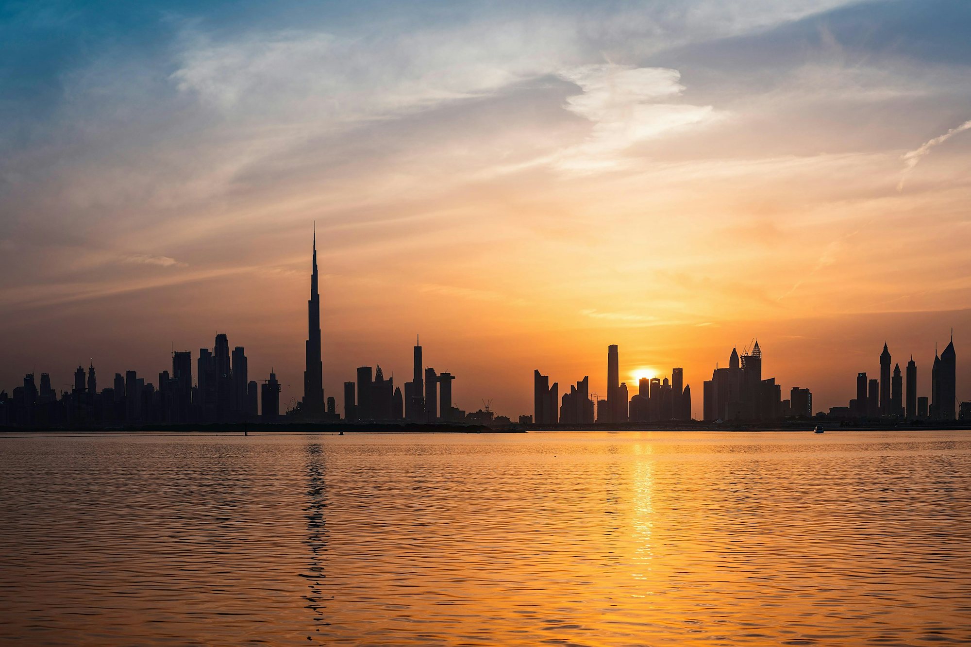 The Dubai skyline and the Burj Khalifa at sunset over the water