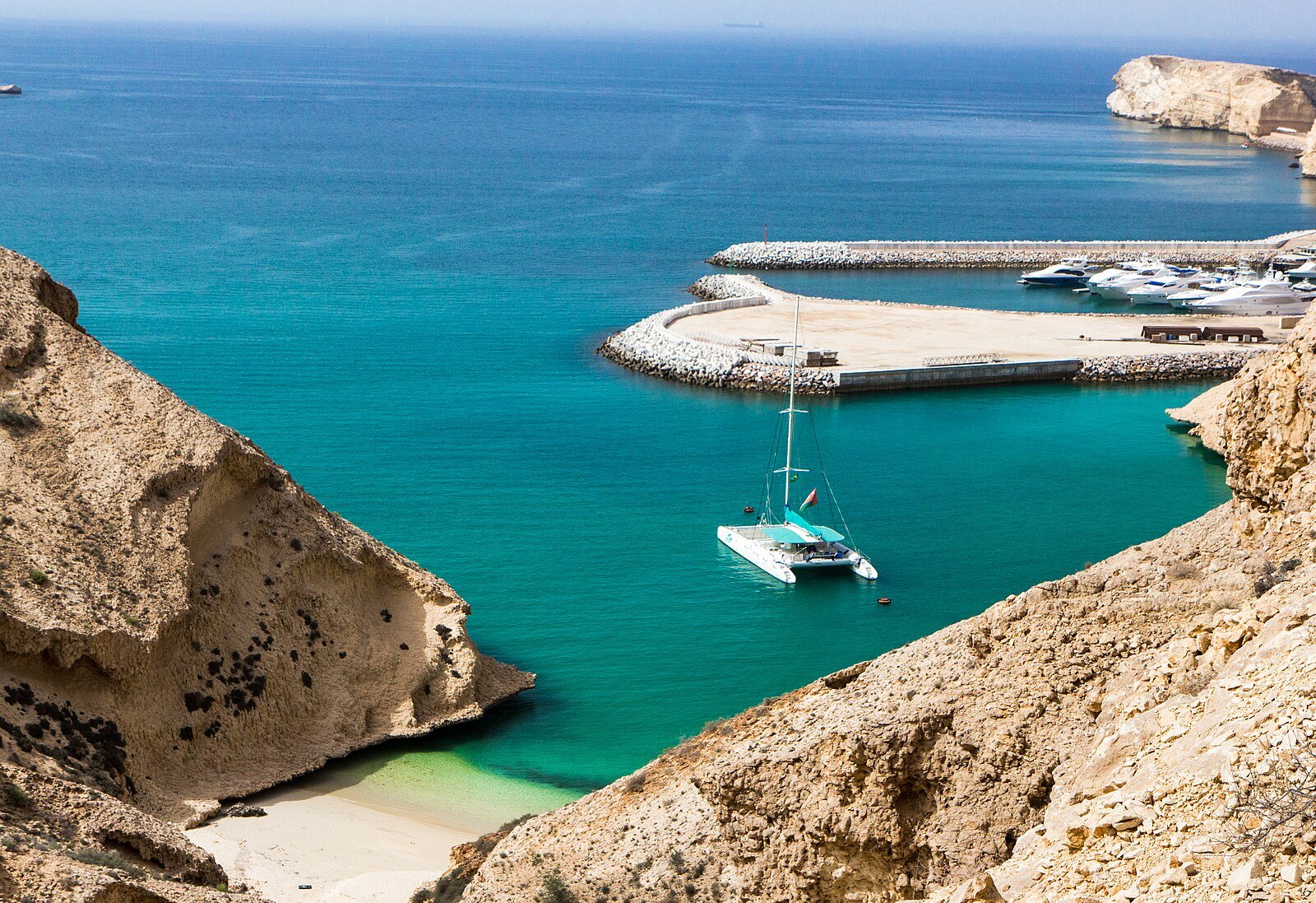 A catamaran anchored in a turquoise cove beside the marina of the Shangri-La Barr Al Jissah resort on the coast of Muscat.