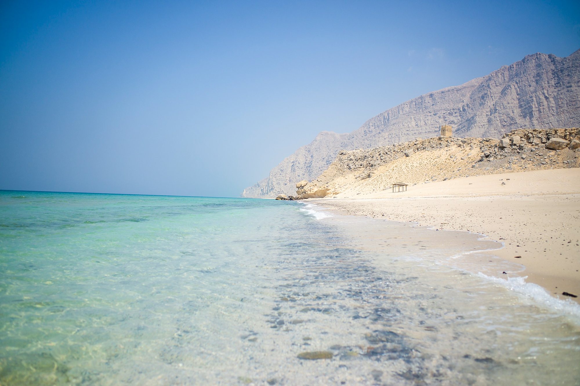 Clear turquoise water on a white beach below the mountains of Musandam, Oman