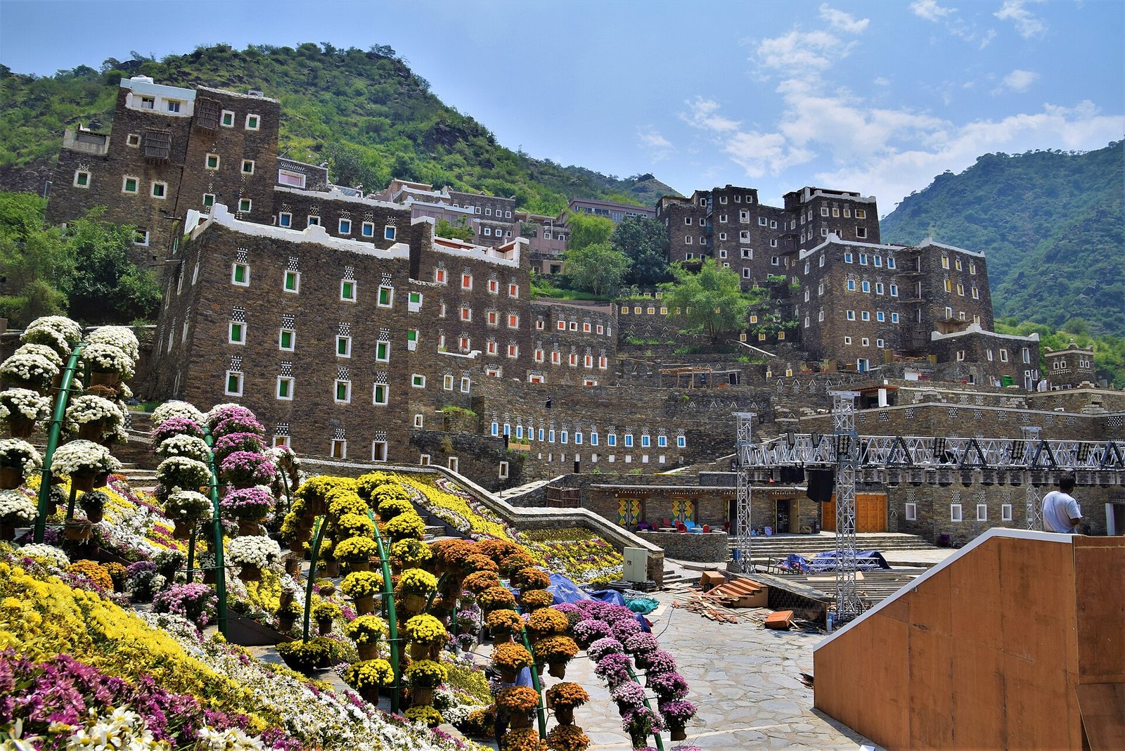 The stone tower houses of Rijal Almaa village rising against green Asir mountains, flowers in bloom below.