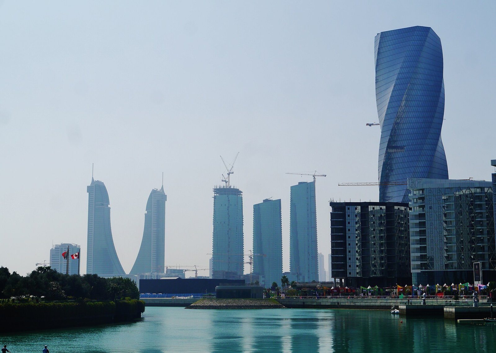The twisting towers of Bahrain Bay reflected in calm water on the Manama waterfront.
