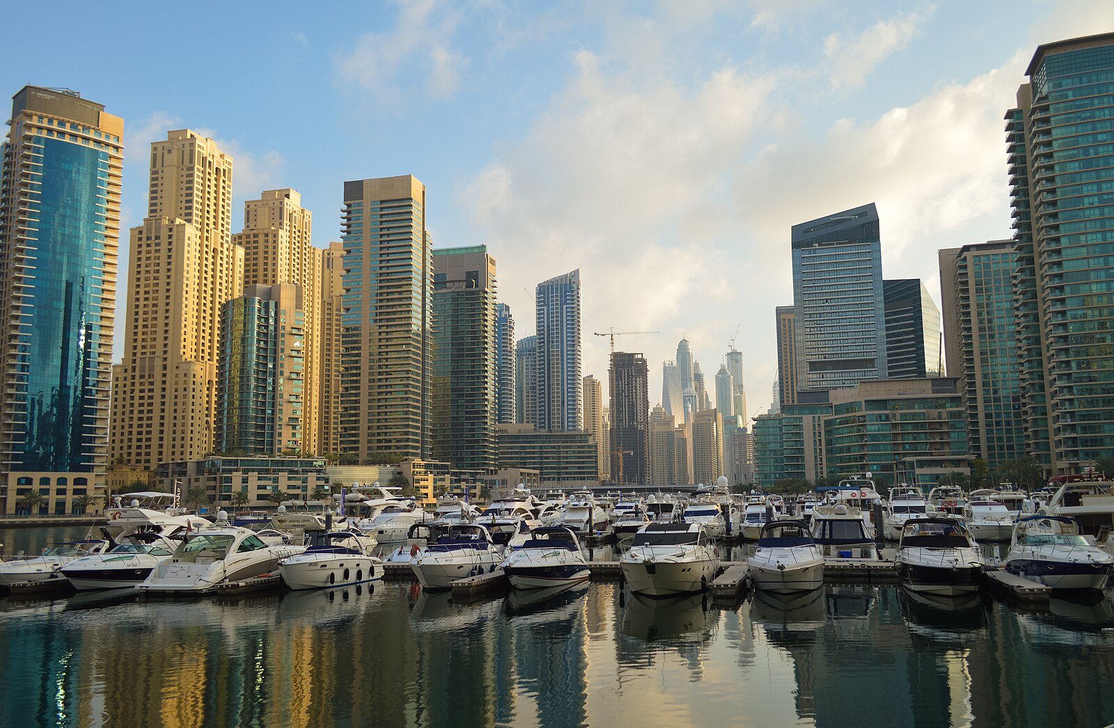 Yachts moored in Dubai Marina beneath its residential towers, reflected in the still water.