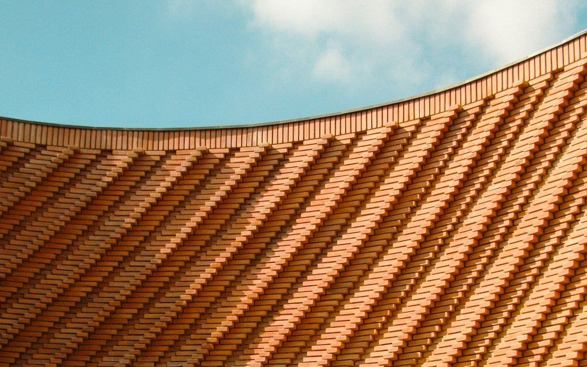 The curving terracotta brick lattice of the Musée Yves Saint Laurent Marrakech sweeps beneath a soft blue sky.