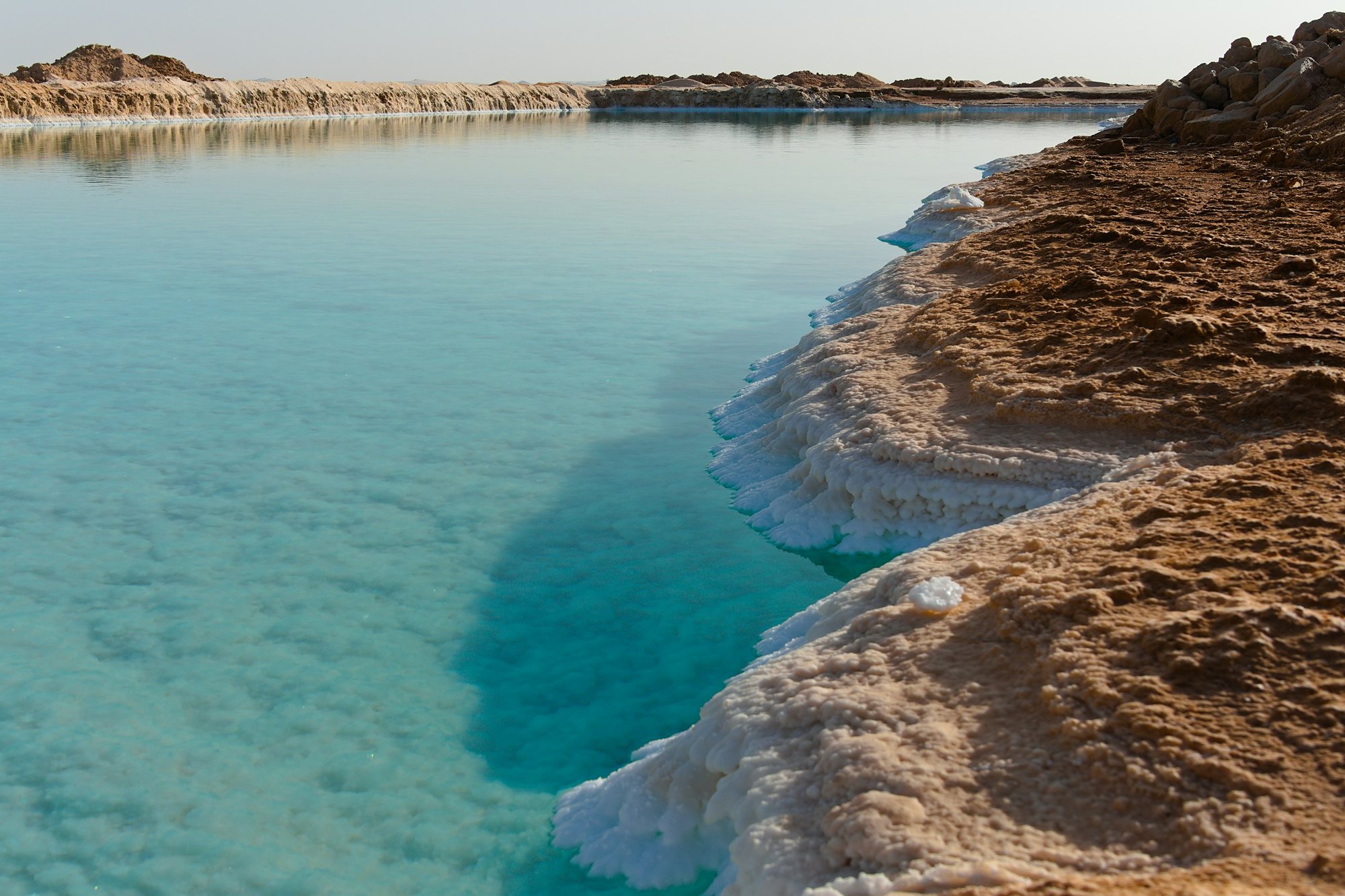 A turquoise salt lake with a crust of white salt at Siwa Oasis, Egypt