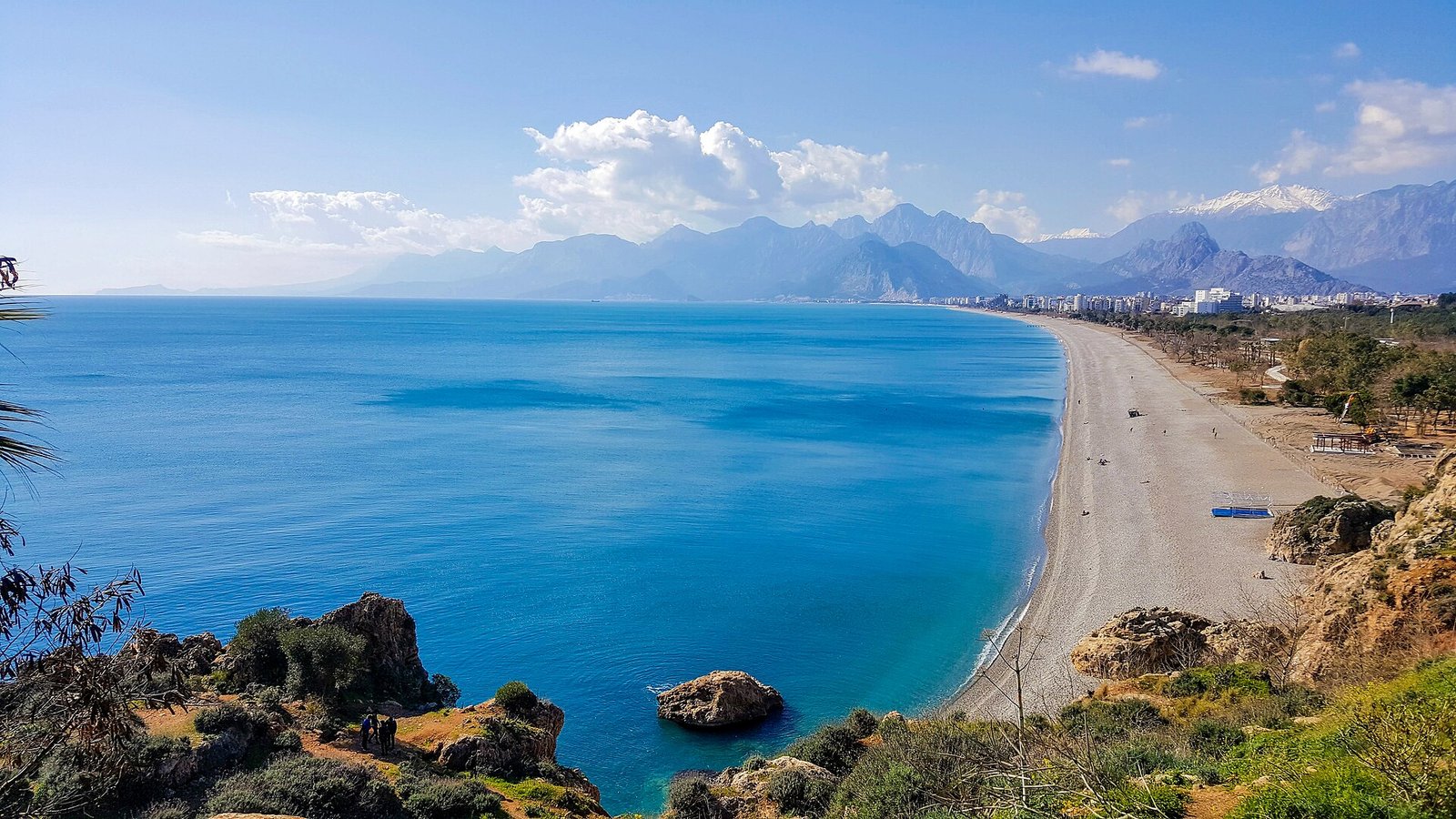 The long curve of Konyaalti Beach and turquoise water below the Bey Mountains, seen from the cliffs of Antalya.