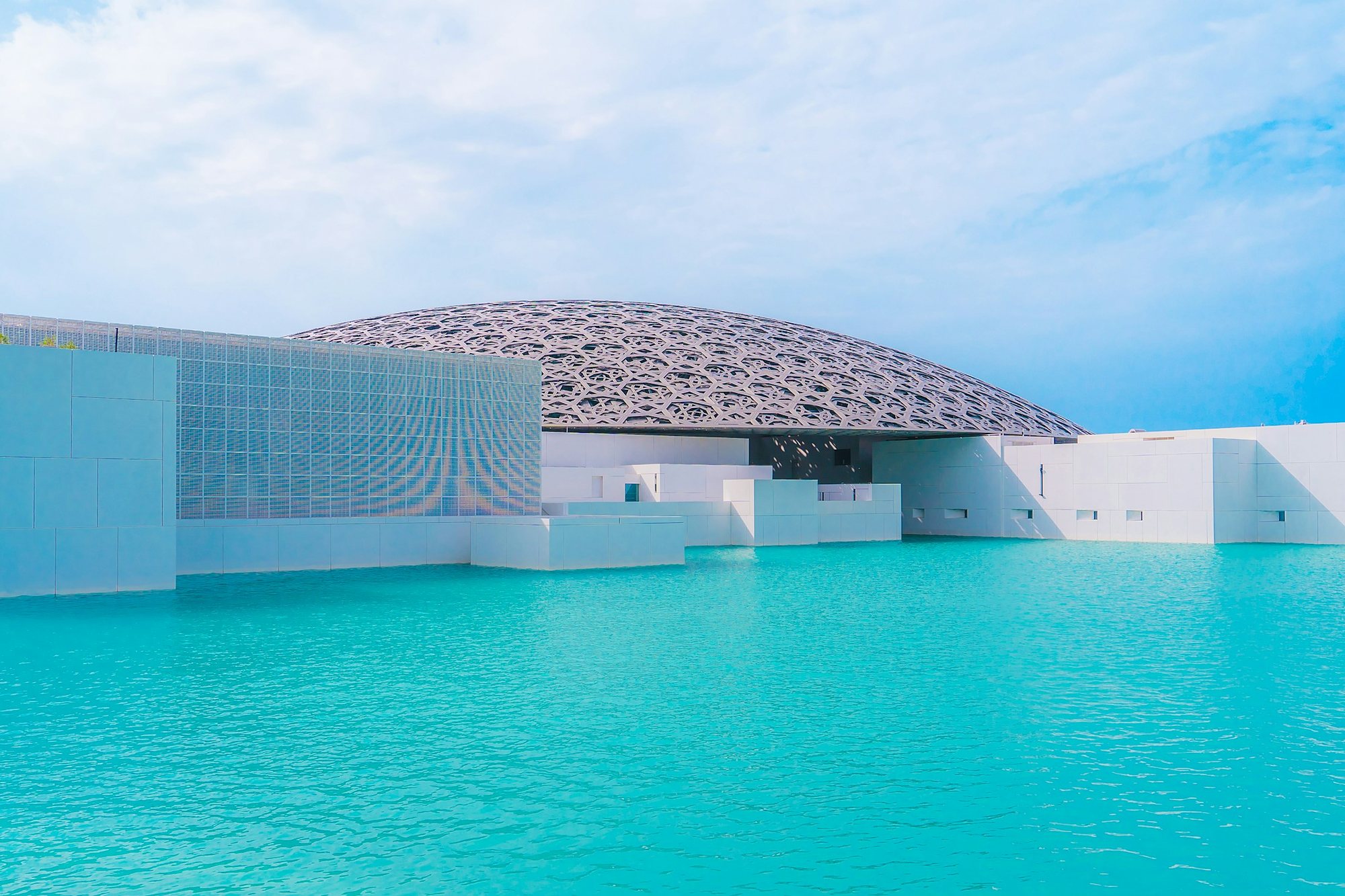 The latticed dome of the Louvre Abu Dhabi above turquoise water on Saadiyat Island