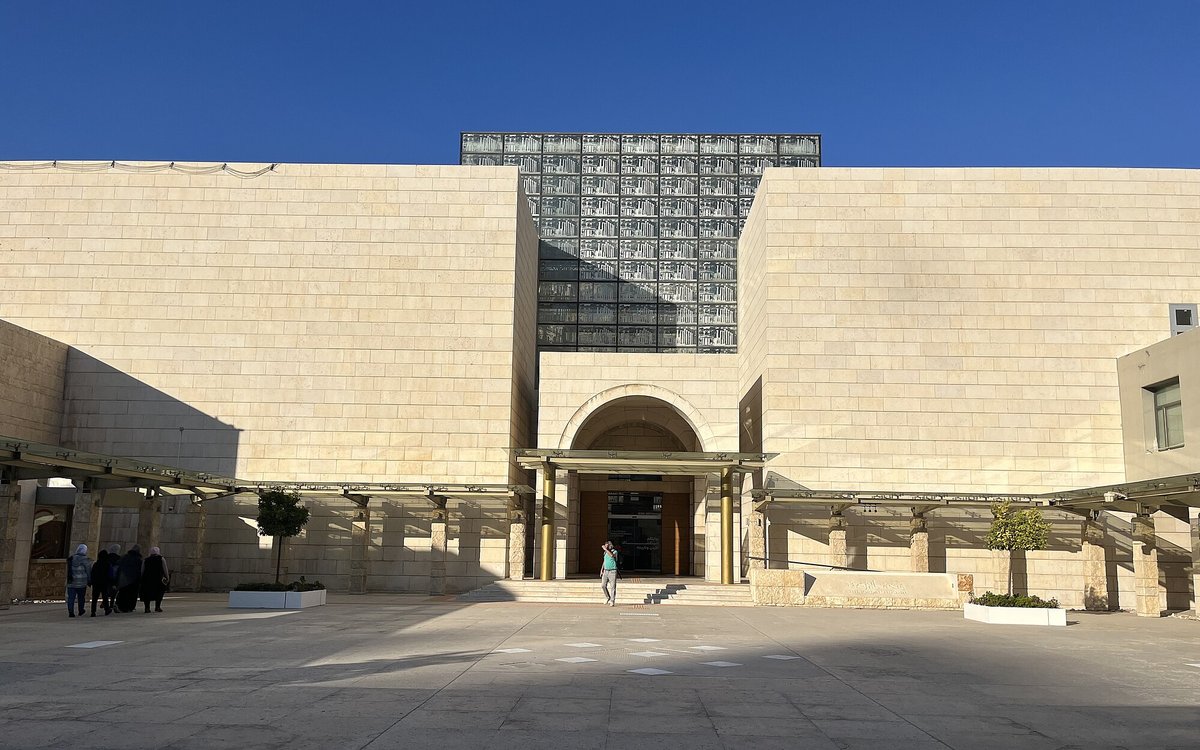 The pale limestone facade and arched entrance of the Jordan Museum in Amman beneath a clear blue sky.