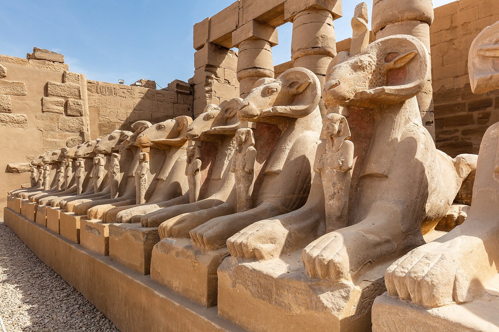 The avenue of ram-headed sphinxes at the Karnak Temple complex in Luxor under a blue sky.
