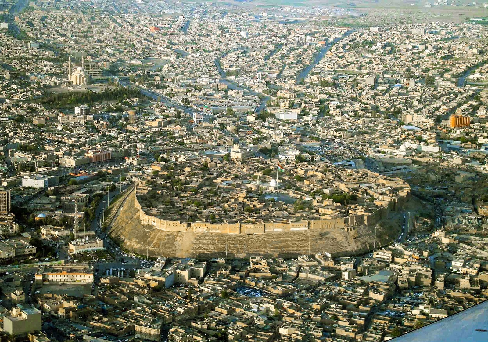The oval ramparts of the ancient Citadel of Erbil rise above the city of Erbil, seen from the air.