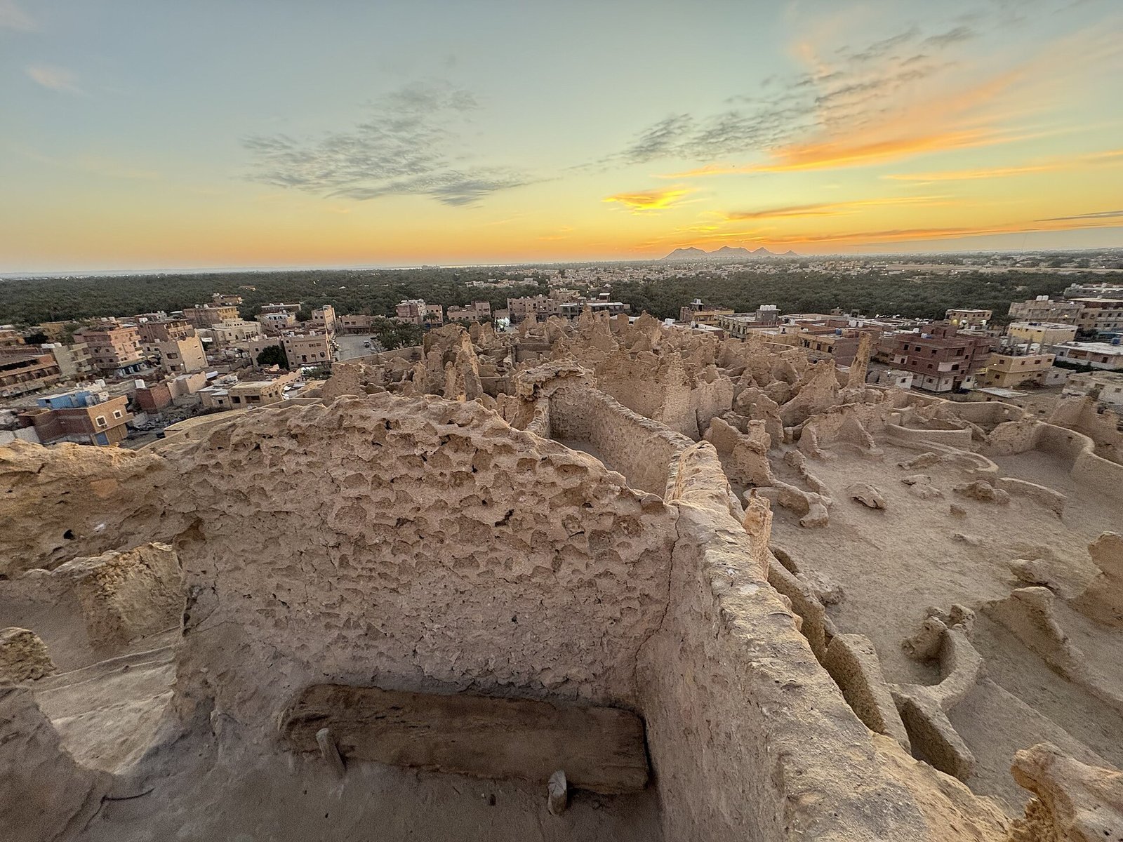The weathered mud-brick ruins of the Shali fortress at Siwa Oasis under a golden sunset sky.