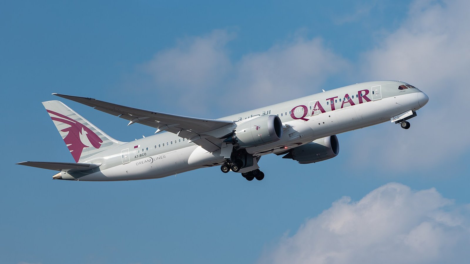 A Qatar Airways Boeing 787 Dreamliner climbing into a bright blue sky after takeoff.
