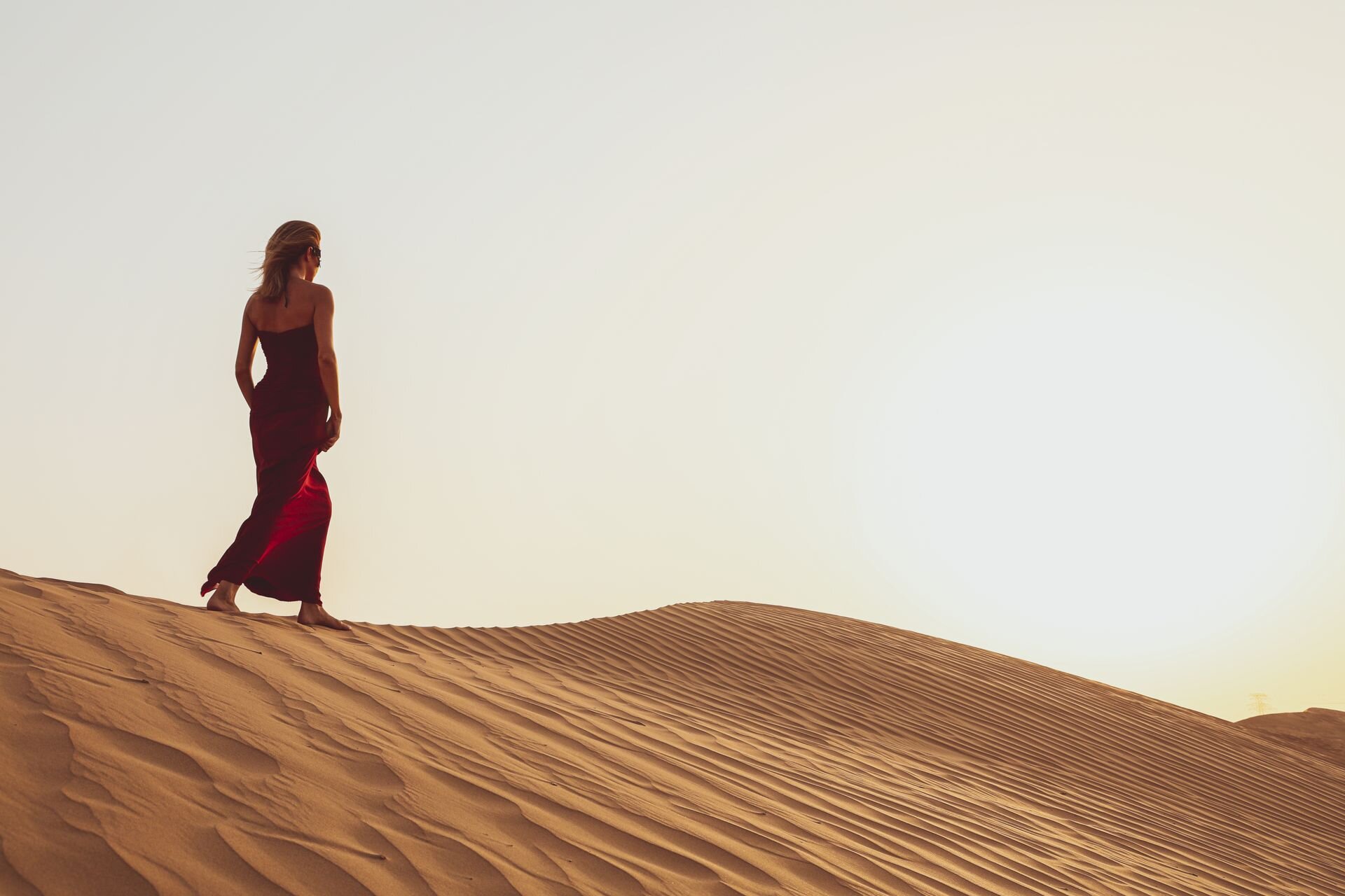 A traveler in a red dress walking the dunes outside Dubai at sunset