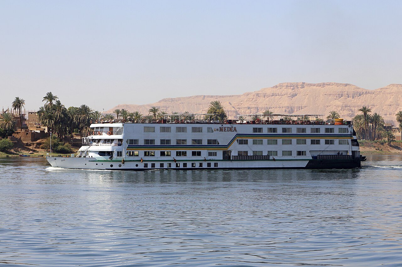 A Nile cruise ship gliding past palms and the Theban hills near Luxor.
