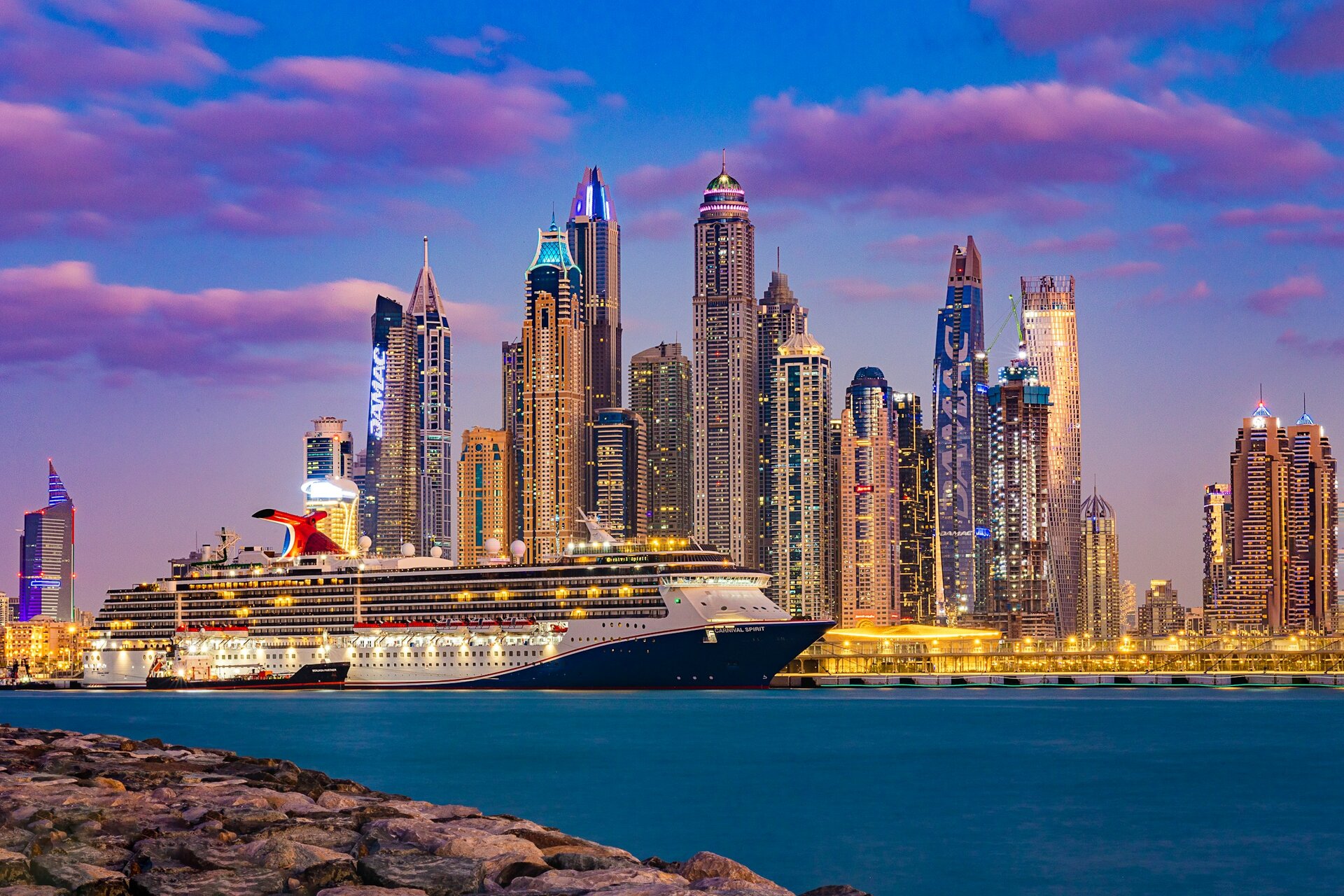 A cruise ship berthed at the Dubai Harbour terminal below the towers of Dubai Marina at dusk