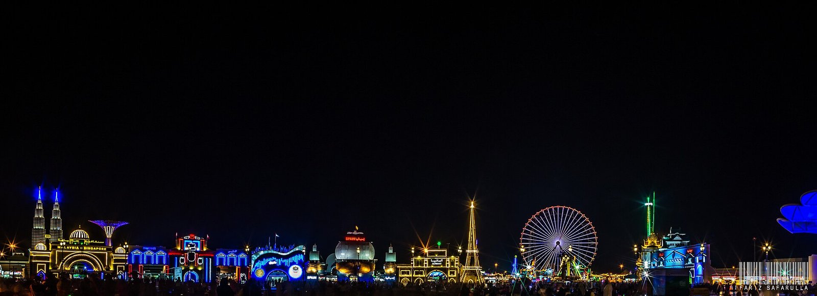 The illuminated pavilions, towers and Ferris wheel of Global Village, Dubai, at night.